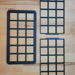 May include: Three black rectangular grid organizers with a uniform square pattern. One large grid is positioned on the left, while two smaller, identical grid inserts are stacked vertically on the right side, all featuring a matte finish.