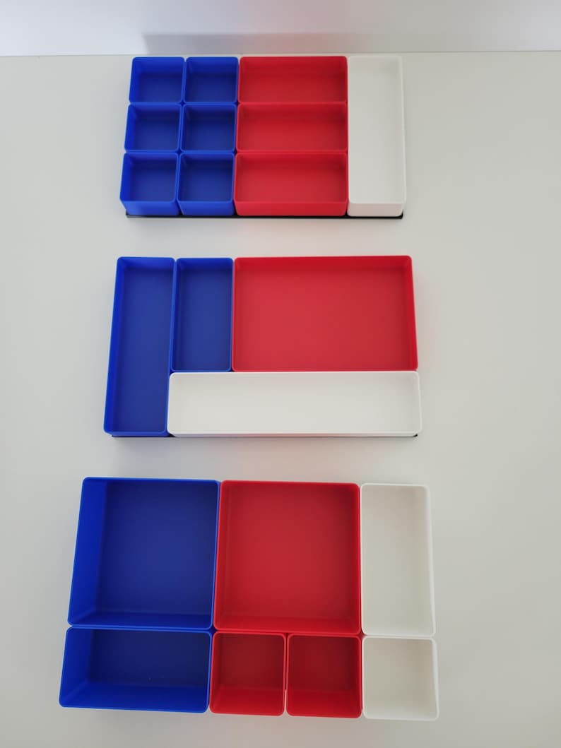 May include: Three rectangular drawer organizer sets featuring modular compartments in solid blue, red, and white plastic. Each set contains various sizes of open-top bins arranged in different configurations to provide segmented storage for small items.
