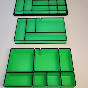 May include: Three rectangular drawer organizers featuring a bright green interior and a black exterior frame. Each organizer contains multiple compartments of varying sizes, designed with straight walls and flat bases for modular storage organization.