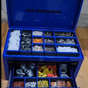 May include: A blue metal toolbox with two drawers. The top drawer is open and contains various small parts organized in compartments. The bottom drawer is closed and has a label that reads "US GENERAL".