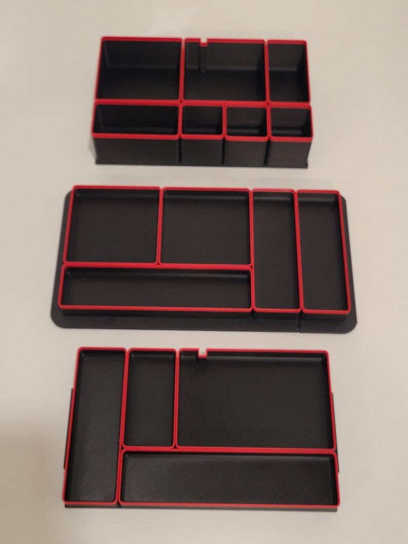 May include: Three black rectangular desk organizers with vibrant red trim. Each organizer features multiple compartments of varying sizes for storage. The design includes clean lines and a structured layout, providing organized sections for small items.