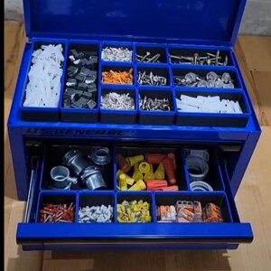 May include: A blue US General metal tool chest with an open lid and one extended drawer. The interior features black plastic organizers filled with various hardware, including white wall anchors, metal screws, wire connectors, and electrical terminals.