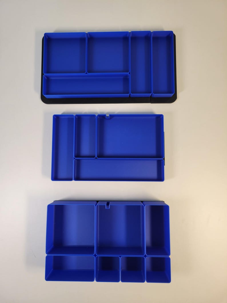 May include: Three rectangular blue plastic drawer organizers with various compartment configurations. Each tray features multiple open sections of different sizes for sorting items, set against a plain background for clear visibility.