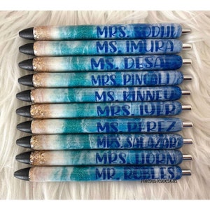 May include: Ten personalized pens with blue and white ocean-themed designs. Each pen has a different name printed on it in blue lettering. The names are: Mrs. Codhu, Ms. Imura, Ms. Desa, Mrs. Pincol, Ms. Kinneu, Mrs. Iyer, Ms. Perez, Mrs. Salazar, Mrs. Horn, Mr. Robles.