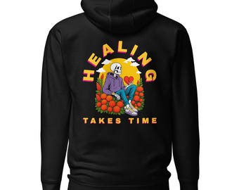 Könnte beinhalten: Schwarzer Kapuzenpullover mit Grafik auf dem Rücken. Die Grafik zeigt ein Skelett mit lila Kapuzenpullover, das ein rotes Herz hält, mit den Worten "HEALING TAKES TIME" in Gelb und Orange. Das Skelett sitzt in einem Feld aus orangefarbenen Blumen.