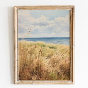 Puede incluir: Una pintura enmarcada de un paisaje marítimo con hierbas altas en primer plano y un océano azul en el fondo. El cielo es de un azul claro con nubes blancas.