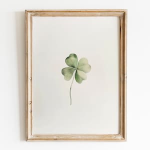 Peut inclure: Une impression encadrée d'une peinture à l'aquarelle d'un trèfle à quatre feuilles avec une tige verte sur un fond blanc.