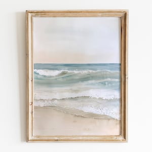 K&ouml;nnte beinhalten: Ein gerahmtes Aquarellbild eines Meeresbildes mit blauen und gr&uuml;nen Wellen, die an einem Sandstrand brechen. Der Himmel ist in sanftem Rosa und Blau gehalten.