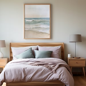 K&ouml;nnte beinhalten: Ein Schlafzimmer mit einem hellrosa Bettbezug und einem Holzbettgestell. &Uuml;ber dem Bett h&auml;ngt ein gerahmtes Bild mit einer Strandszene, und es gibt zwei Nachttische mit Lampen.
