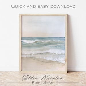 K&ouml;nnte beinhalten: Ein Aquarellbild von Ozeanwellen, die an einem Sandstrand brechen. Das Bild ist in einem hellen Holzrahmen gerahmt und h&auml;ngt an einer wei&szlig;en Wand.