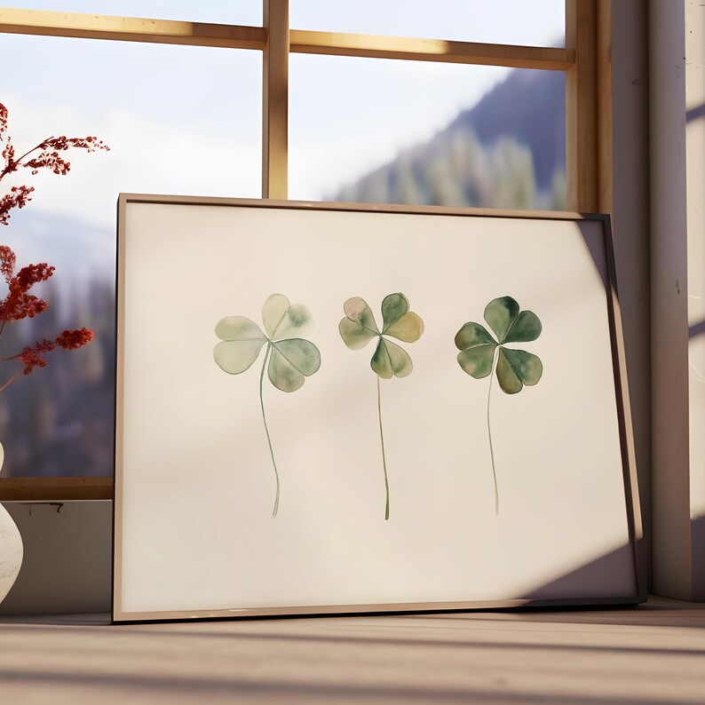 May include: A framed watercolor painting of three green four-leaf clovers on a white background.