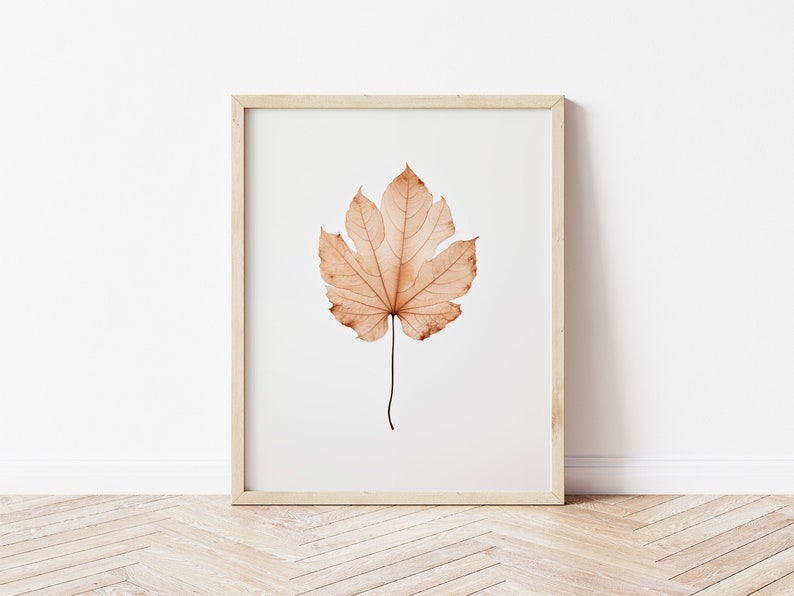 May include: A framed print featuring a detailed, dried leaf in shades of brown and tan. The leaf is centered on a white background, encased in a light-colored wooden frame. The artwork evokes a sense of nature and autumn.