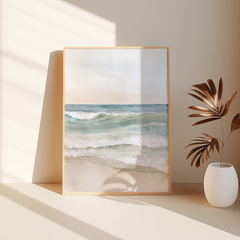 K&ouml;nnte beinhalten: Ein gerahmtes Aquarellbild eines Meeresbildes mit blauen und wei&szlig;en Wellen, die an einem Sandstrand brechen. Das Bild hat eine weiche, vertr&auml;umte Atmosph&auml;re und ist perfekt f&uuml;r ein Zuhause im K&uuml;sten-Stil.