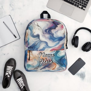 May include: A backpack with a swirling abstract design in shades of blue, pink, and orange. The front pocket features the text "Name Here" in a script font. The backpack has a black handle and zipper.
