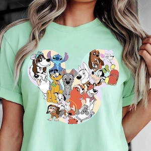 May include: A mint green t-shirt with a graphic of cartoon dogs in a Mickey Mouse head shape. The design includes characters like Stitch and Pluto. The shirt is labelled "Bella Canvas Mint color". It is a crew neck style. The shirt is made of a soft material.