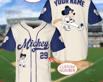 May include: A cream and navy blue baseball jersey featuring a button-down front, the script text Mickey, and the number 29. The back displays the text YOUR NAME above a graphic of Mickey Mouse holding a baseball bat, with navy blue sleeves.