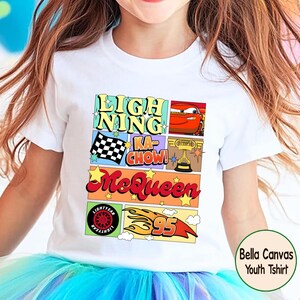 Puede incluir: Camiseta blanca para ni&ntilde;os con un dise&ntilde;o gr&aacute;fico colorido. El dise&ntilde;o incluye el texto "Lightning Ka-Chow! McQueen", un coche de carreras, una bandera a cuadros, un trofeo y el n&uacute;mero 95. La camiseta tambi&eacute;n tiene el texto "Lightyear".