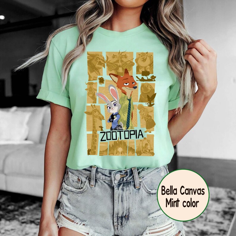 May include: A mint green t-shirt featuring a graphic from the Disney movie Zootopia. The design includes characters Judy Hopps and Nick Wilde, along with other characters in a grid pattern. The text "ZOOTOPIA" is below the characters.