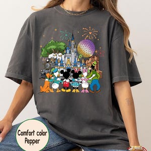 Peut inclure: T-shirt gris fonc&eacute; Comfort Colors avec un motif color&eacute; de personnages Disney devant un ch&acirc;teau, une grande sph&egrave;re et des feux d'artifice. Le texte "Comfort color Pepper" est imprim&eacute; sur le t-shirt.