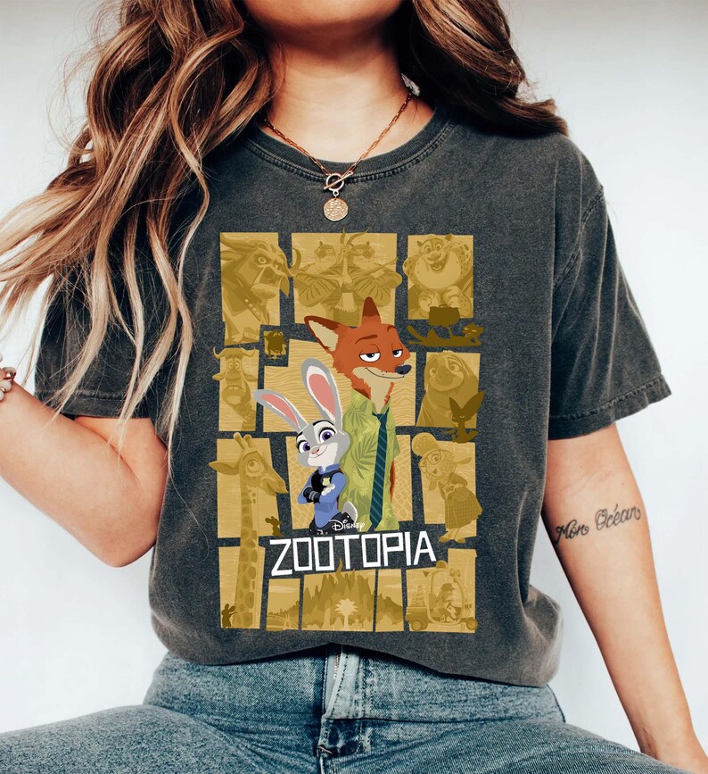 May include: Dark gray t-shirt featuring the word "ZOOTOPIA" with cartoon characters Nick Wilde and Judy Hopps. The shirt has a distressed look and a collage of Zootopia characters in the background.