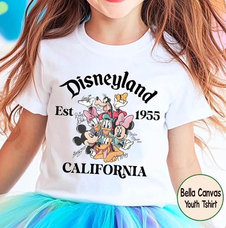 May include: White youth t-shirt featuring a colorful graphic of Disney characters, including Mickey Mouse, Minnie Mouse, and Donald Duck. The shirt has the text "Disneyland Est 1955 California".