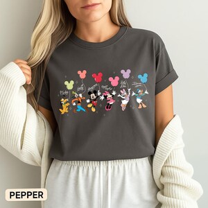 K&ouml;nnte beinhalten: Dunkelgraues T-Shirt mit einem farbenfrohen Aufdruck von Disney-Figuren, die Mickey Mouse-f&ouml;rmige Ballons halten. Pluto, Goofy, Mickey, Minnie, Daisy und Donald sind abgebildet. Das Wort "Pepper" ist unten aufgedruckt.