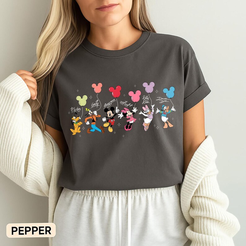 K&ouml;nnte beinhalten: Dunkelgraues T-Shirt mit einem farbenfrohen Aufdruck von Disney-Figuren, die Mickey Mouse-f&ouml;rmige Ballons halten. Pluto, Goofy, Mickey, Minnie, Daisy und Donald sind abgebildet. Das Wort "Pepper" ist unten aufgedruckt.