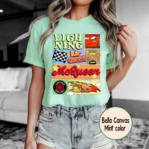 Puede incluir: Camiseta verde menta con un dise&ntilde;o gr&aacute;fico colorido. El dise&ntilde;o incluye el texto "LIGHTNING KA-CHOW! McQueen" junto con im&aacute;genes de un coche de carreras, una bandera a cuadros y el n&uacute;mero 95. Fabricada en Bella Canvas.