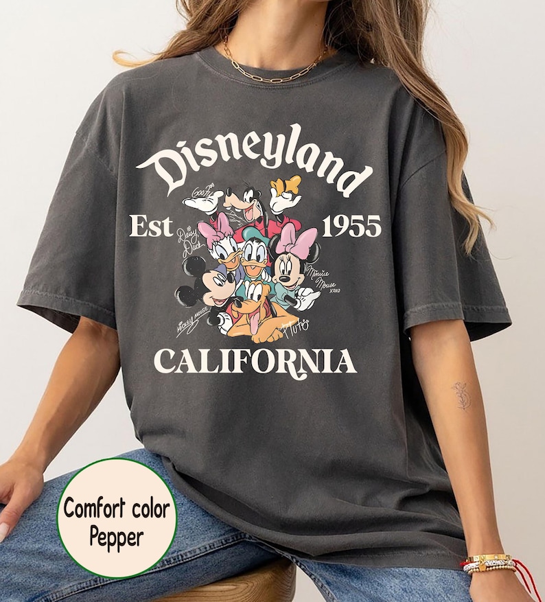 May include: Dark gray t-shirt with the text "Disneyland California Est. 1955" and cartoon characters. The shirt features Mickey Mouse, Minnie Mouse, Donald Duck, Daisy Duck, Goofy, and Pluto. The shirt is a comfort color pepper.
