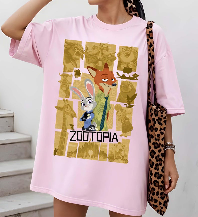 May include: A light pink t-shirt featuring a graphic from the Disney movie Zootopia. The design includes characters Judy Hopps and Nick Wilde, with the movie title in bold letters. The shirt has short sleeves and a relaxed fit.