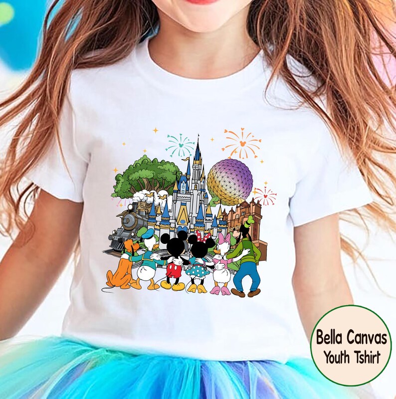 Peut inclure: T-shirt blanc pour enfant avec un graphisme color&eacute; de personnages Disney devant un ch&acirc;teau, un train et une sph&egrave;re. Le motif comprend des feux d'artifice et le texte "Bella Canvas Youth Tshirt".