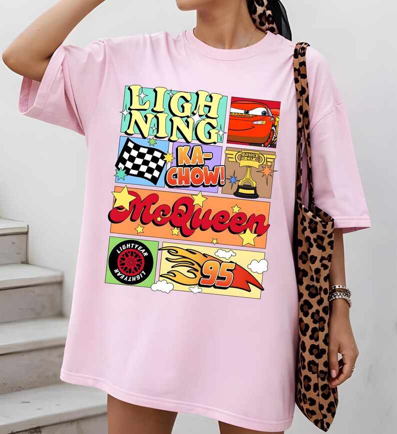 Puede incluir: Camiseta rosa claro con un dise&ntilde;o gr&aacute;fico colorido. El dise&ntilde;o incluye el texto "LIGHTNING KA-CHOW! McQueen" junto con im&aacute;genes de un coche de carreras, una bandera a cuadros, un trofeo, un neum&aacute;tico y el n&uacute;mero 95. La camiseta es de corte holgado.