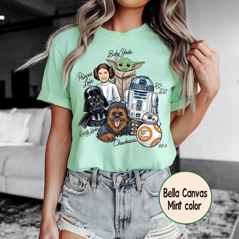 May include: Mint green t-shirt featuring Star Wars characters: Darth Vader, Princess Leia, Baby Yoda, Chewbacca, R2-D2, and BB-8. The shirt has the text "Bella Canvas Mint color".