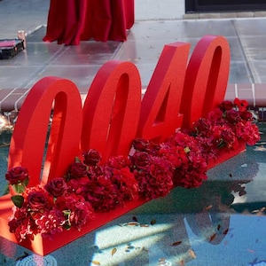 May include: Large red numbers spelling out "0040" are displayed in a pool, decorated with red roses and other red flowers. The numbers are placed on a red base. A red tablecloth is visible in the background.