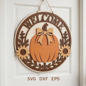 May include: A circular wooden door sign featuring the word WELCOME in dark brown letters at the top. The center displays an orange pumpkin with a light tan bow. Two sunflowers and leafy vine accents in brown and tan surround the pumpkin. The text SVG DXF EPS is printed at the bottom.