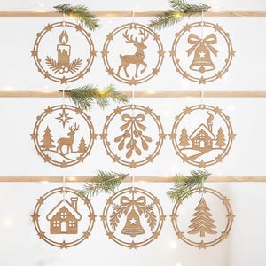 Op de afbeelding: Een set van negen ronde houten ornamenten met lasergesneden ontwerpen, waaronder een kaars, rendier, bel, maretak, huis en dennenboom. Elk ornament is omlijst door een ring met kleine steraccenten en hangt aan een houten stang.