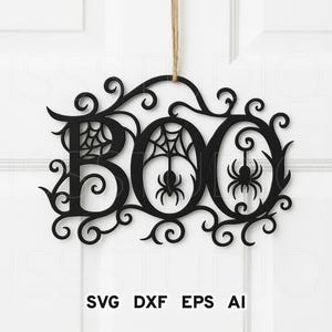 May include: A black laser-cut hanging sign featuring the word BOO in a decorative font with swirling flourishes. The letter O contains a spider web and a spider, while the second O features a hanging spider. It hangs from a tan twine string.