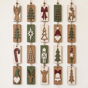 May include: A set of twenty rectangular wooden ornaments arranged in four vertical columns, each featuring laser-cut holiday icons like trees, reindeer, angels, gnomes, and candy canes in shades of forest green, deep red, white, and natural wood.