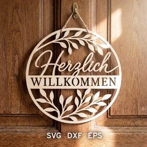 Può includere: Un cartello rotondo in legno con le parole "Herzlich Willkommen" intagliate in un carattere decorativo, circondato da un design floreale. Il cartello è appeso a una porta di legno. La parte inferiore del cartello riporta la scritta "SVG DXF EPS".