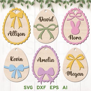 Peut inclure: Six décorations en bois en forme d'œuf de Pâques avec des bords festonnés. Chaque décoration présente un nom différent, "Allison", "David", "Nora", "Kevin", "Amelia" et "Megan", ainsi qu'un nœud de couleur différente.