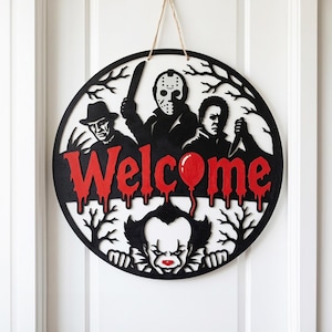 Puede incluir: Un letrero de pared circular de madera negra con la palabra Welcome en letras rojas que parecen gotear. El diseño incluye siluetas recortadas de tres personajes de películas de terror, un globo rojo y ramas de árboles desnudas, colgado de un cordel.