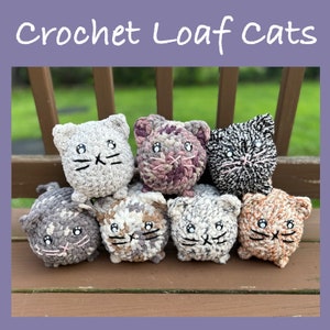 May include: Seven crocheted loaf cats in various colors and patterns, including gray, purple, black, brown, and white, sitting on a wooden bench. The cats have black eyes and whiskers.