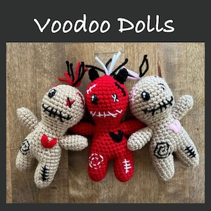 May include: Three crocheted voodoo dolls. One is red with black eyes and stitching, one is beige with red heart and black stitching, and one is beige with pink heart and black stitching.