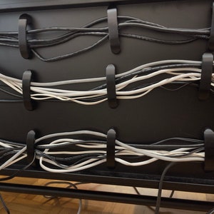 Op de afbeelding: Een close-up van een zwart kabelbeheersysteem met meerdere zwarte en witte kabels die zijn vastgezet met plastic clips.