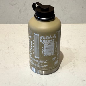 Puede incluir: Una gran botella de agua de acero inoxidable de color beige con una tapa negra y un diseño blanco de un circuito impreso en el lateral.