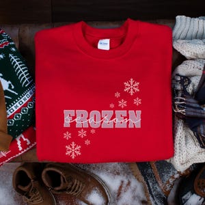 May include: Red sweatshirt with white text that says "Frozen Season" and white snowflake designs.