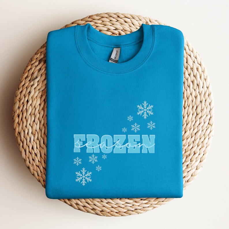 May include: A turquoise blue sweatshirt with the text "FROZEN season" in white with a snowflake design.
