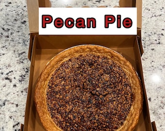 Könnte beinhalten: Ein Pecan Pie in einer Pappbox mit einem durchsichtigen Plastikdeckel. Auf der Box steht "Pecan Pie" gedruckt.