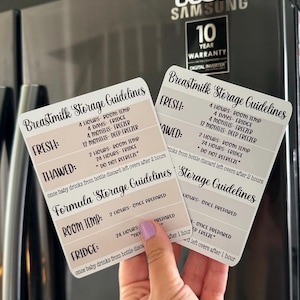 May include: Two laminated cards with storage guidelines for breast milk and formula. The cards are printed with black text on a white background with a light brown accent. The cards are held in a hand.