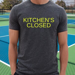May include: A dark gray t-shirt with the text "KITCHEN'S CLOSED" in yellow.
